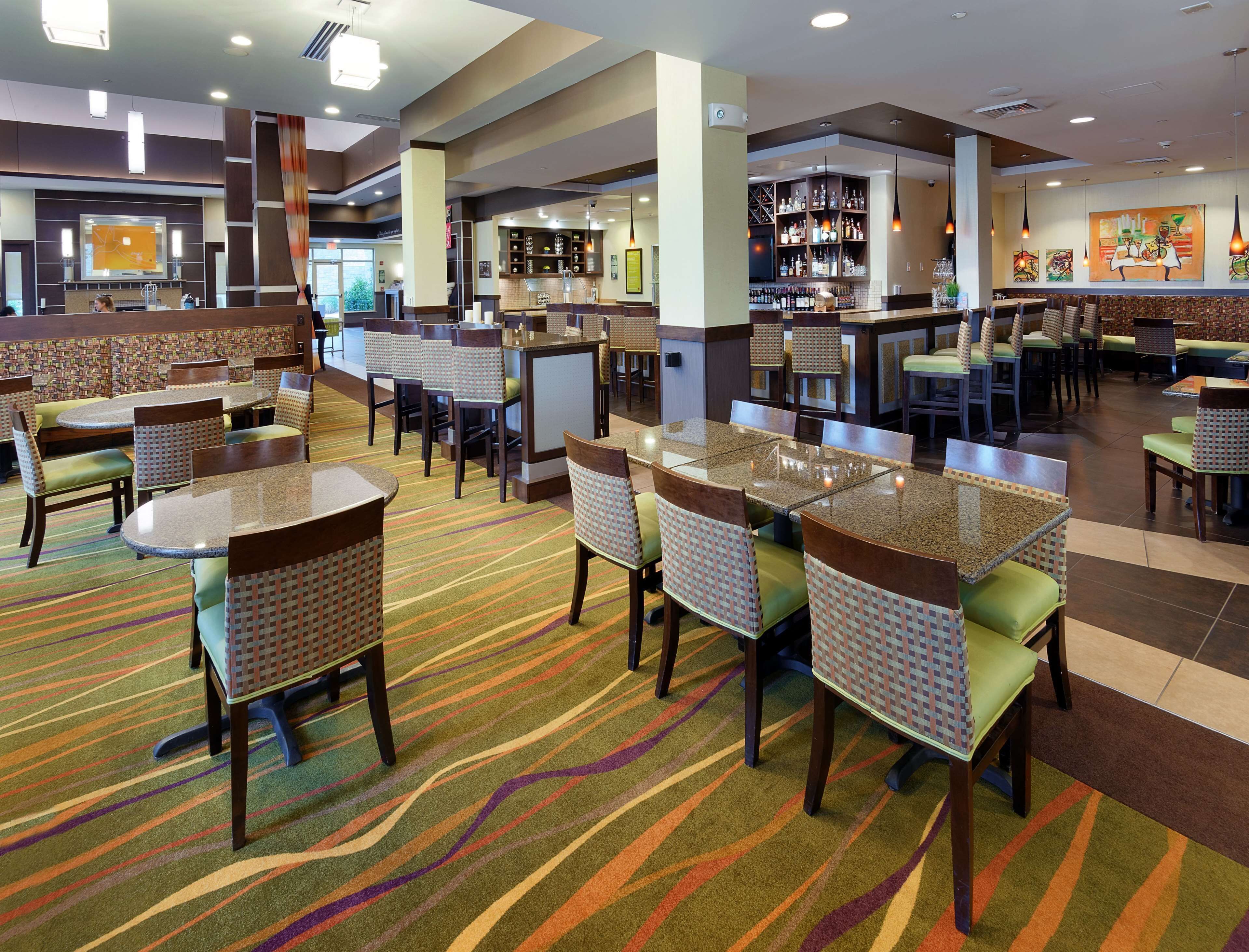 A hotel lobby with multiple seating areas, including round tables and booths, and a bar area with shelves of bottles.