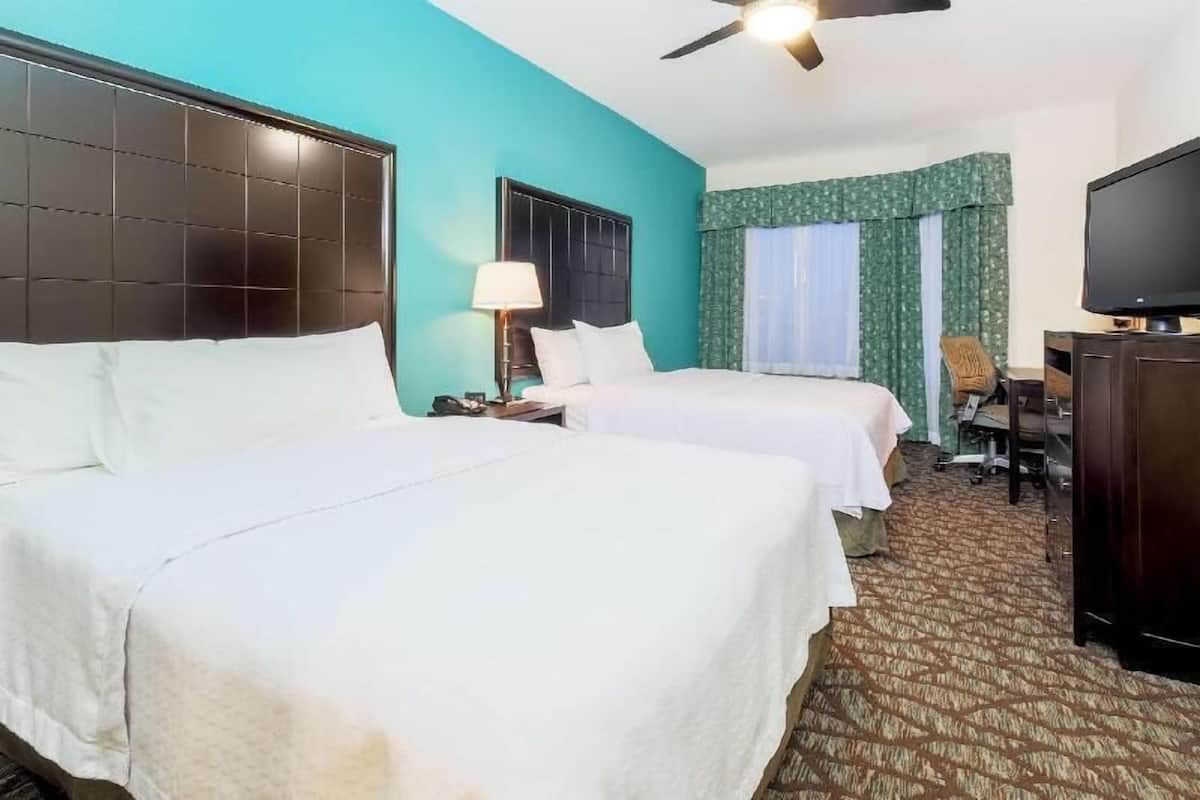 Una habitación de hotel con dos camas, ventilador de techo, televisión y escritorio con silla.