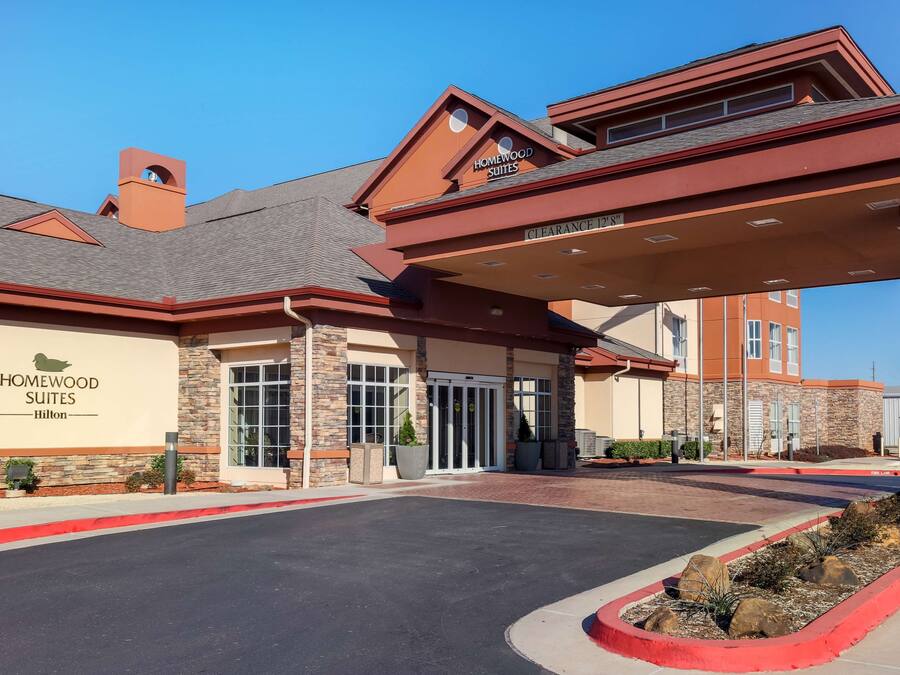 A hotel entrance with a covered driveway, clear signage for Homewood Suites, and a clear sky.