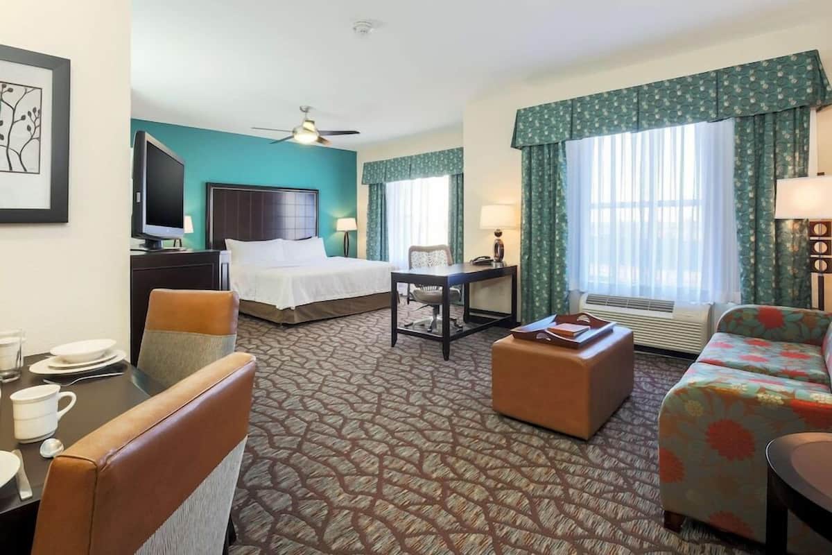 A hotel room with a bed, a desk, a chair, a sofa, a TV, and a dining table with chairs.