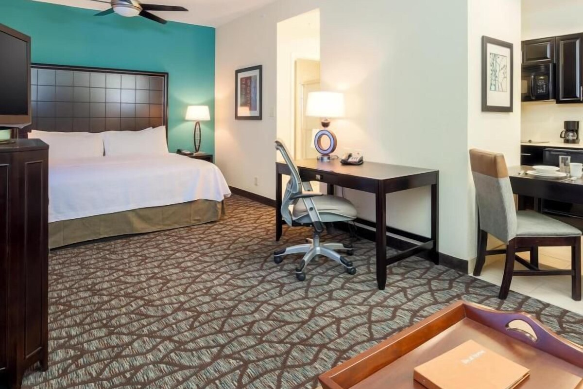 Ein Hotelzimmer mit Bett, Schreibtisch, Stuhl und einer kleinen Küchenzeile.