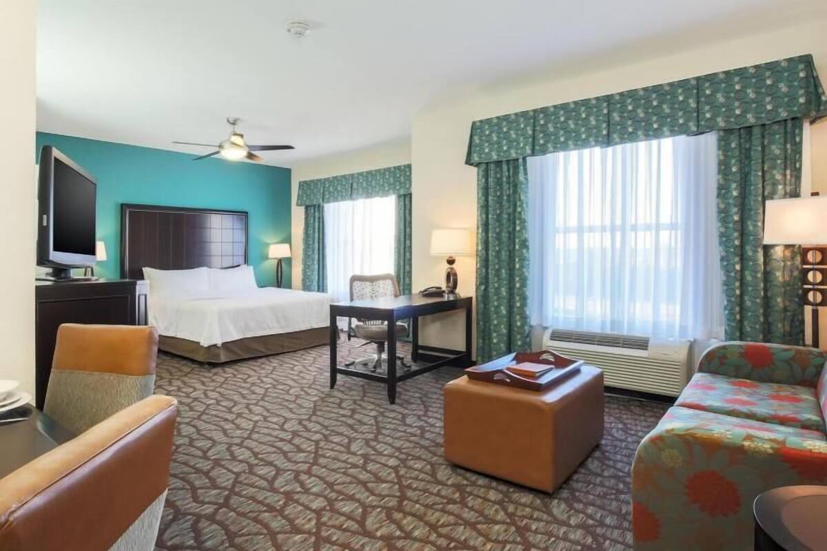 Habitación de hotel con cama, escritorio, silla, reposapiés, sofá, televisor y ventilador de techo.