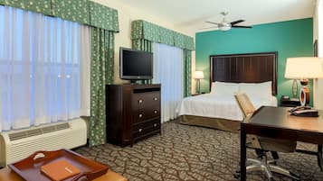 Habitación de hotel con cama, escritorio, silla, televisor, lámpara de escritorio, teléfono, mesita con bandeja, una pequeña mesa con un libro y una ventana con cortinas.
