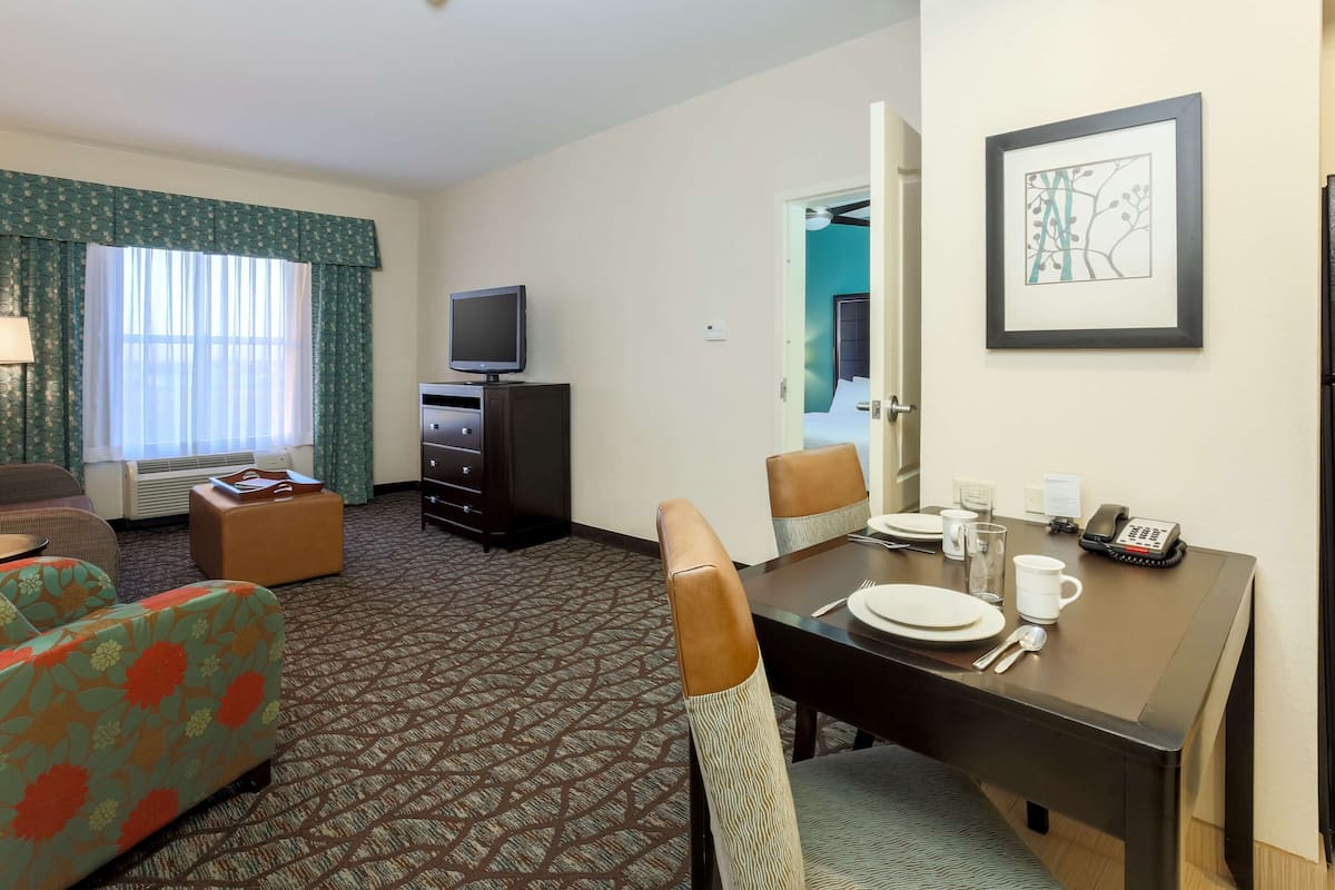 A hotel room with a dining area, a television, a dresser, and a framed artwork on the wall.