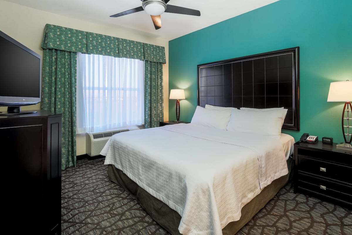 A hotel room with a large bed, a flat-screen TV, a ceiling fan, and a window with curtains.