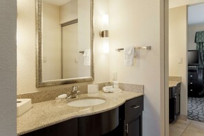 Une salle de bain d’hôtel avec un grand miroir, deux lavabos, un porte-serviettes et un meuble-lavabo doté d’un placard foncé.