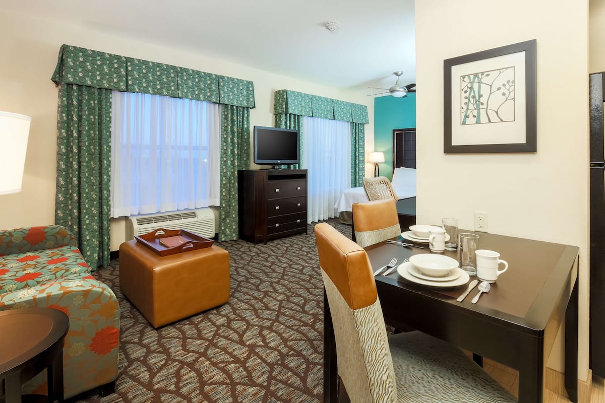 A hotel room with a bed, a TV, a dining table set, and a sofa.