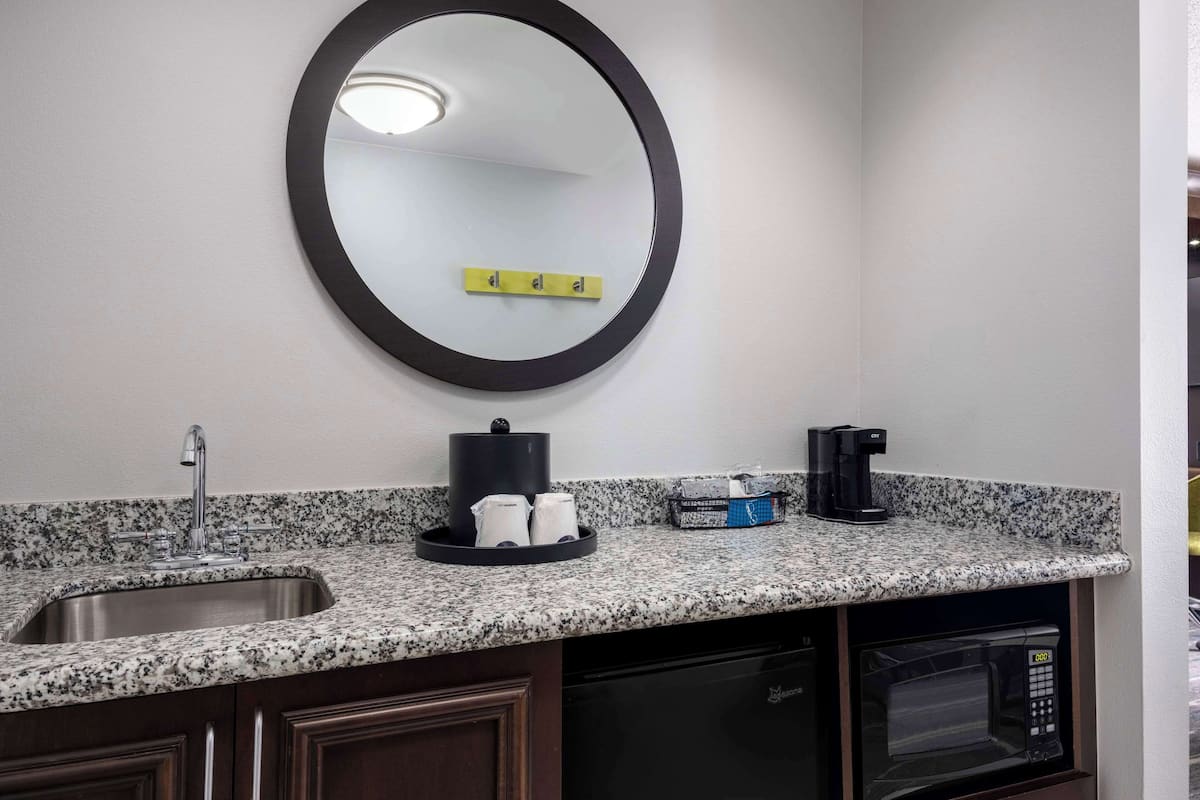 A kitchen with a granite countertop, a sink, a coffee maker, a microwave, and a dish rack.