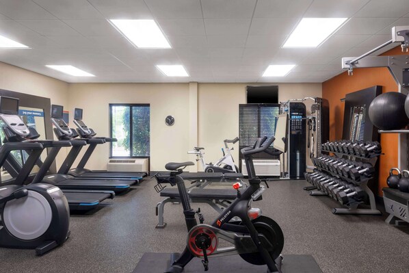 A gym with treadmills, an elliptical, a stationary bike, and a rack of dumbbells.