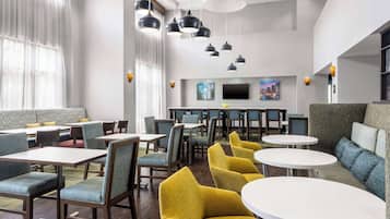 A modern dining area with multiple seating options, including tables and chairs, and a television in the background.