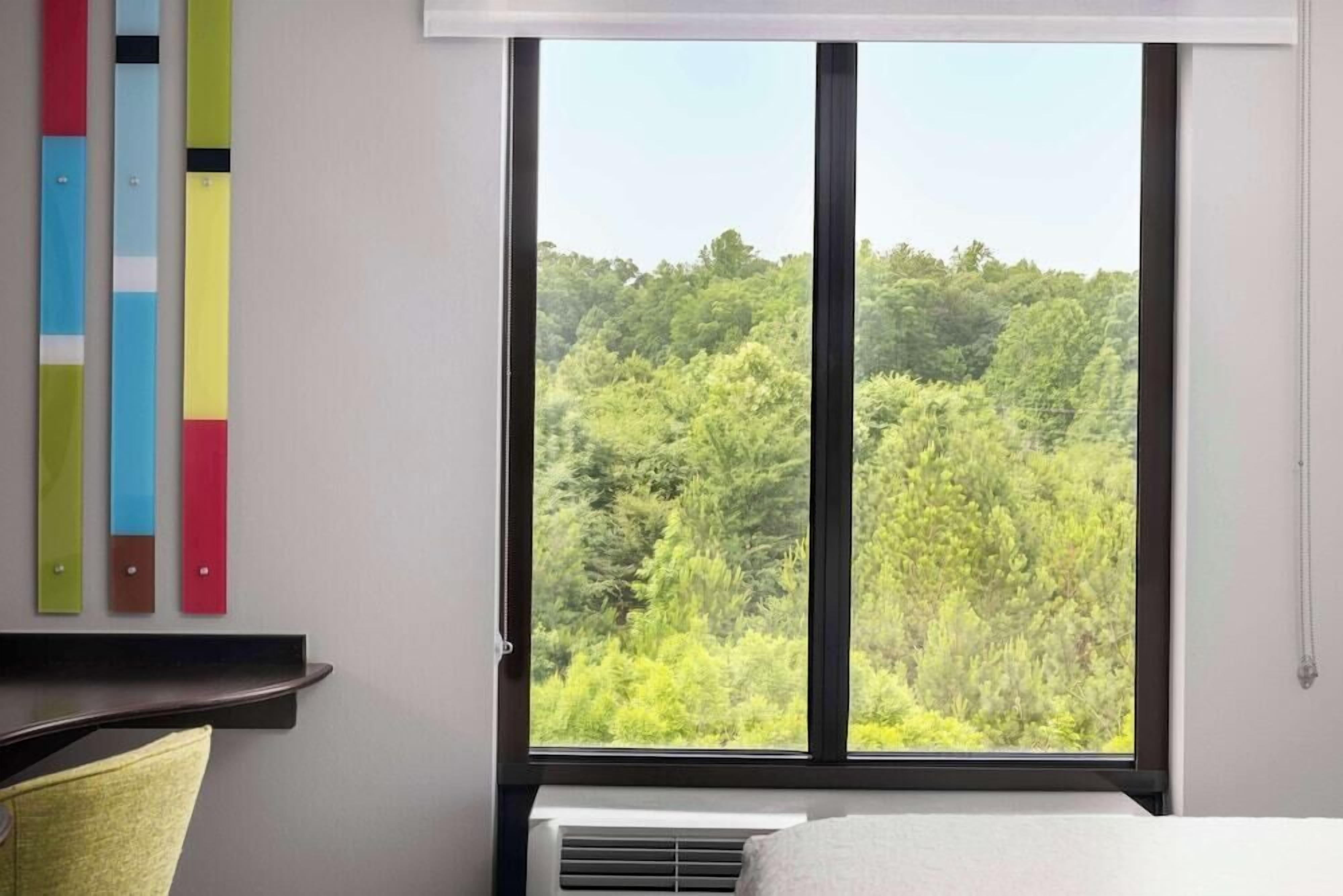 Ein Zimmer mit großem Fenster, einem Bett, einem Schreibtisch und einer Wand-Klimaanlage.