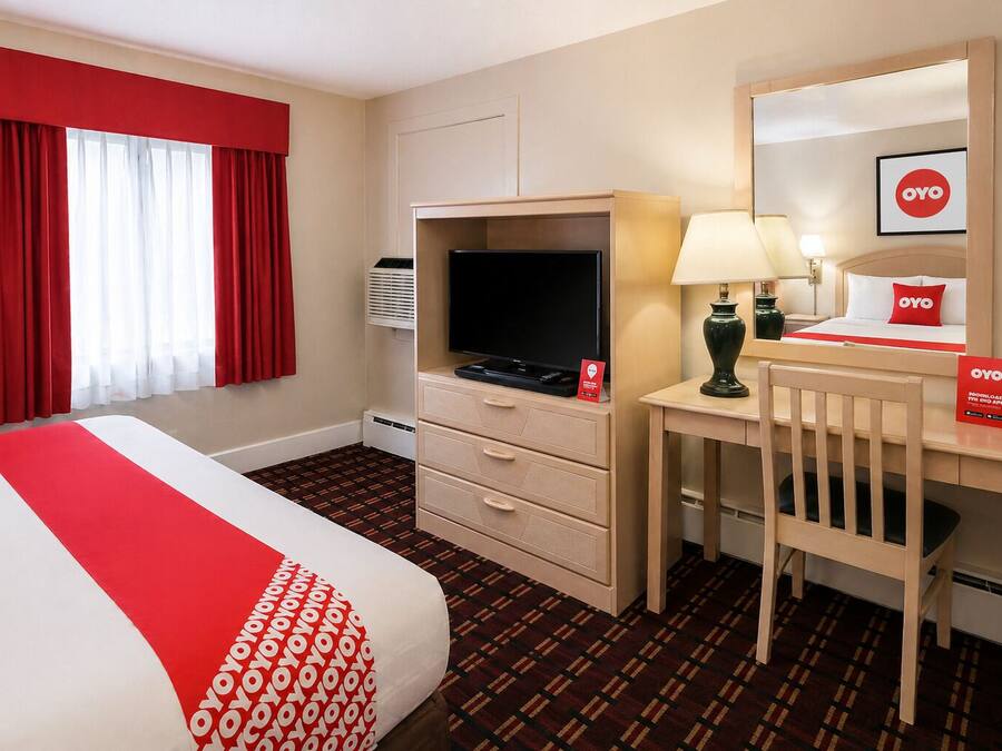 A hotel room with a bed, a desk, a television, a lamp, and a mirror.