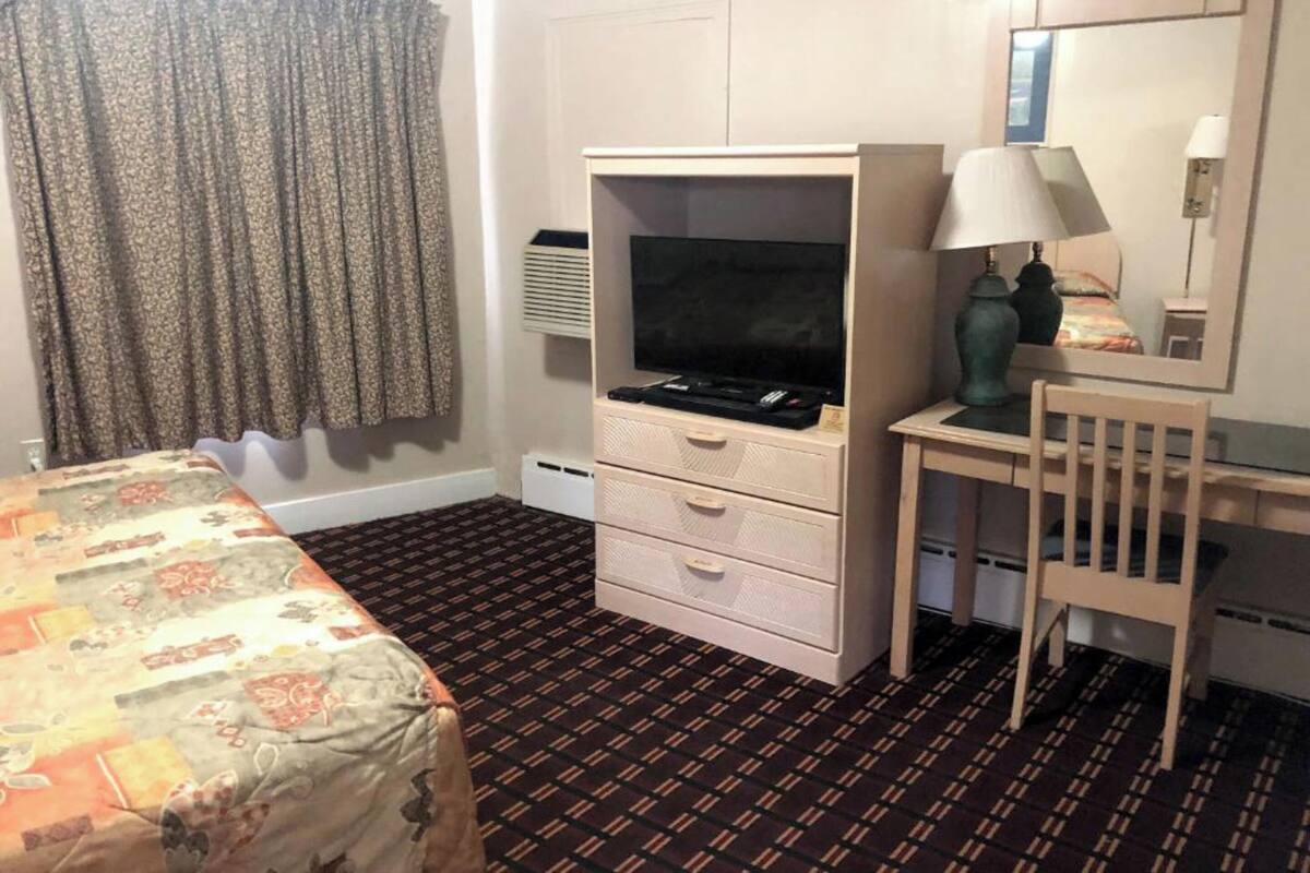 A hotel room with a bed, a desk with a lamp, a television, and a dresser.
