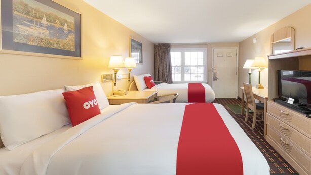 A hotel room with two beds, a desk, a television, and a painting on the wall. - OYO Hotel Starlite Seneca Falls (Seneca Falls)