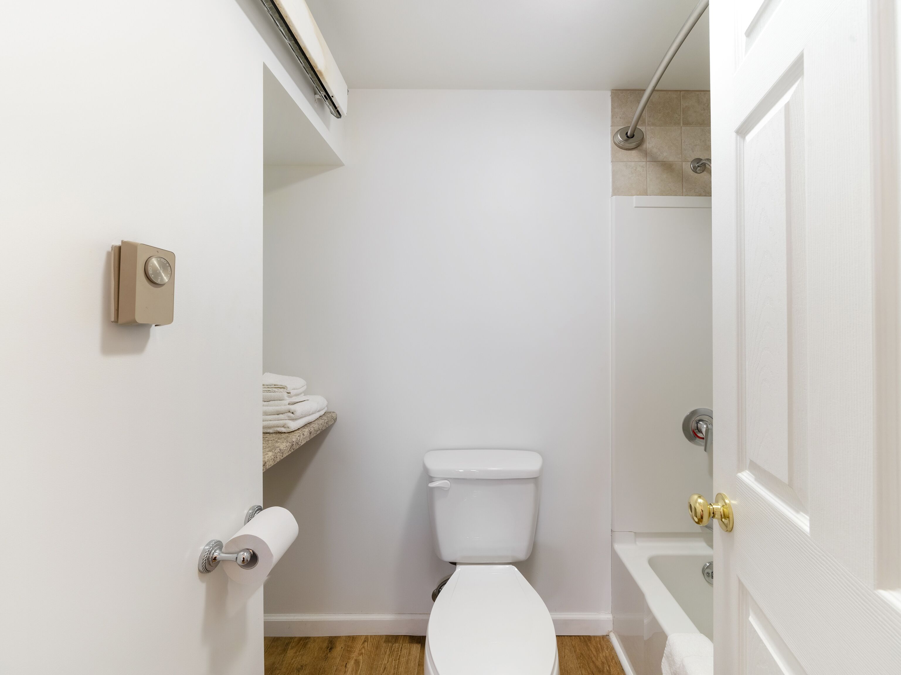 A small, clean bathroom with a toilet, a towel rack, and a shower area.