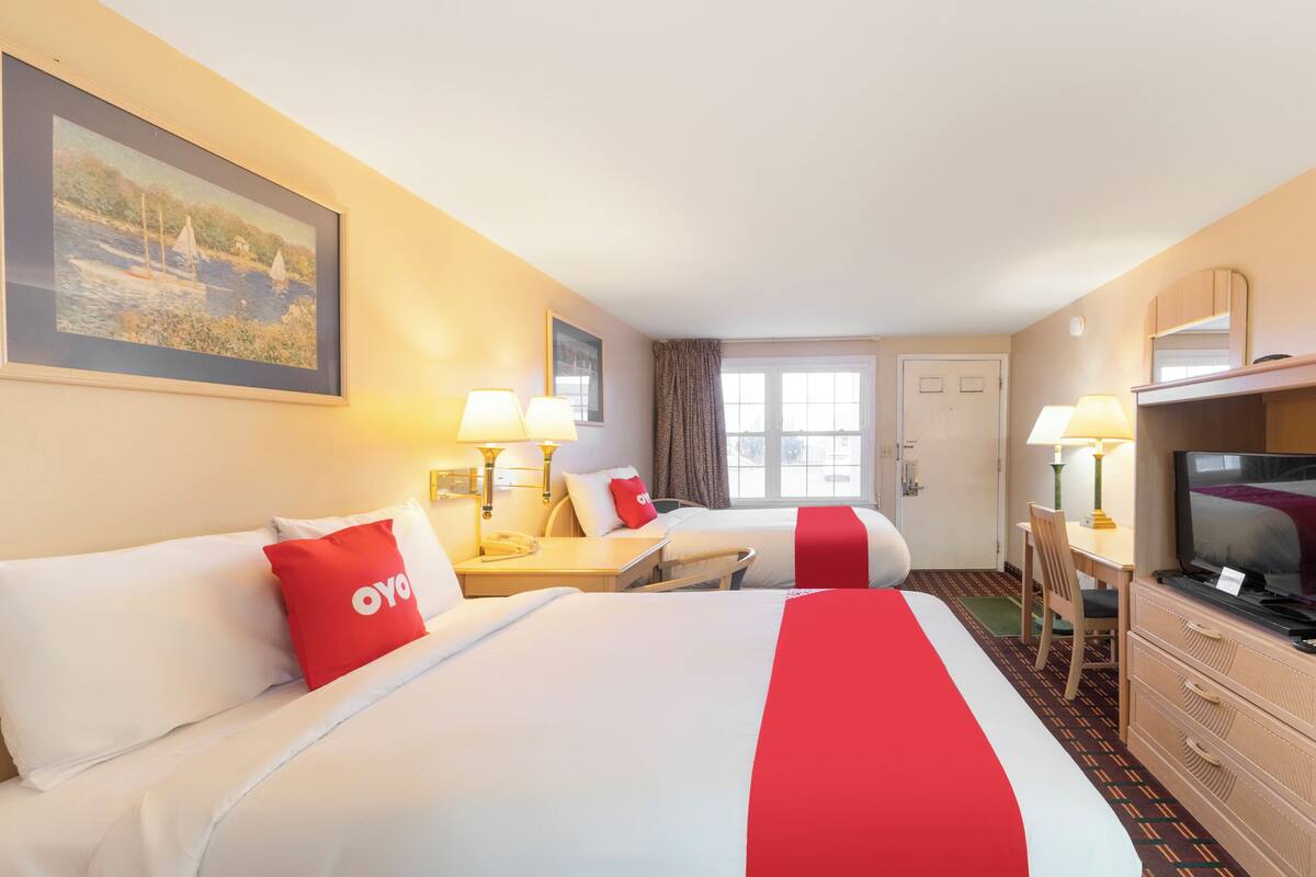 A hotel room with two beds, a desk, a television, and a painting on the wall.