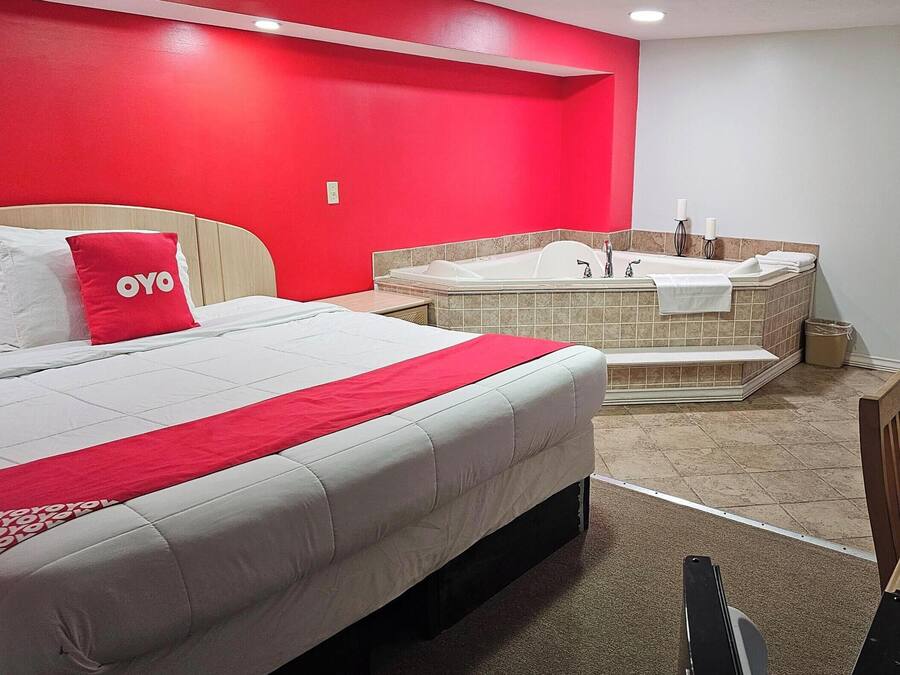 Une chambre d’hôtel avec un grand lit, un mur rouge, un jacuzzi et un plafond blanc.
