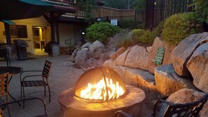 A fire pit with chairs around it, a stone wall, and a sign in the background. - GetAways at Olympic Village Inn (Olympic Valley)