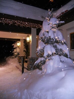 A snow-covered Christmas tree with lights, set against a house with a porch and string lights overhead. - GetAways at Olympic Village Inn (Olympic Valley)