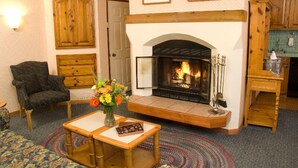 A cozy living room with a fireplace, a wooden cabinet, a chair, and a table with a vase of flowers. - GetAways at Olympic Village Inn (Olympic Valley)