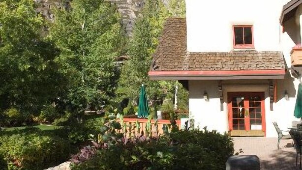 A white building with a stone roof and a small tower, surrounded by greenery and a rocky hillside. - GetAways at Olympic Village Inn (Olympic Valley)