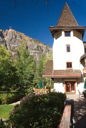 A white building with a stone roof and a small tower, surrounded by greenery and a rocky hillside. - GetAways at Olympic Village Inn (Olympic Valley)
