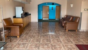 A hotel lobby with a reception desk, a seating area with leather sofas, and a blue elevator. - Tropicana Inn and Suites (Dallas)