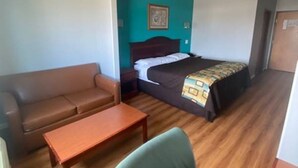 A hotel room with a bed, a sofa, a small table, and a wooden floor. - Tropicana Inn and Suites (Dallas)