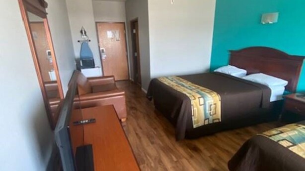 A hotel room with a bed, a desk, a chair, a mirror, and a door. - Tropicana Inn and Suites (Dallas)