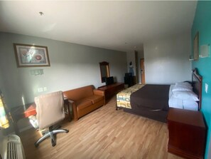 A hotel room with a bed, a sofa, a desk, a chair, a mirror, and a television. - Tropicana Inn and Suites (Dallas)