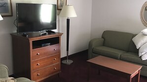 A hotel room with a television on a wooden cabinet, a floor lamp, a green sofa, and a small table. - Laketree Inn And Suites Marion (Marion)