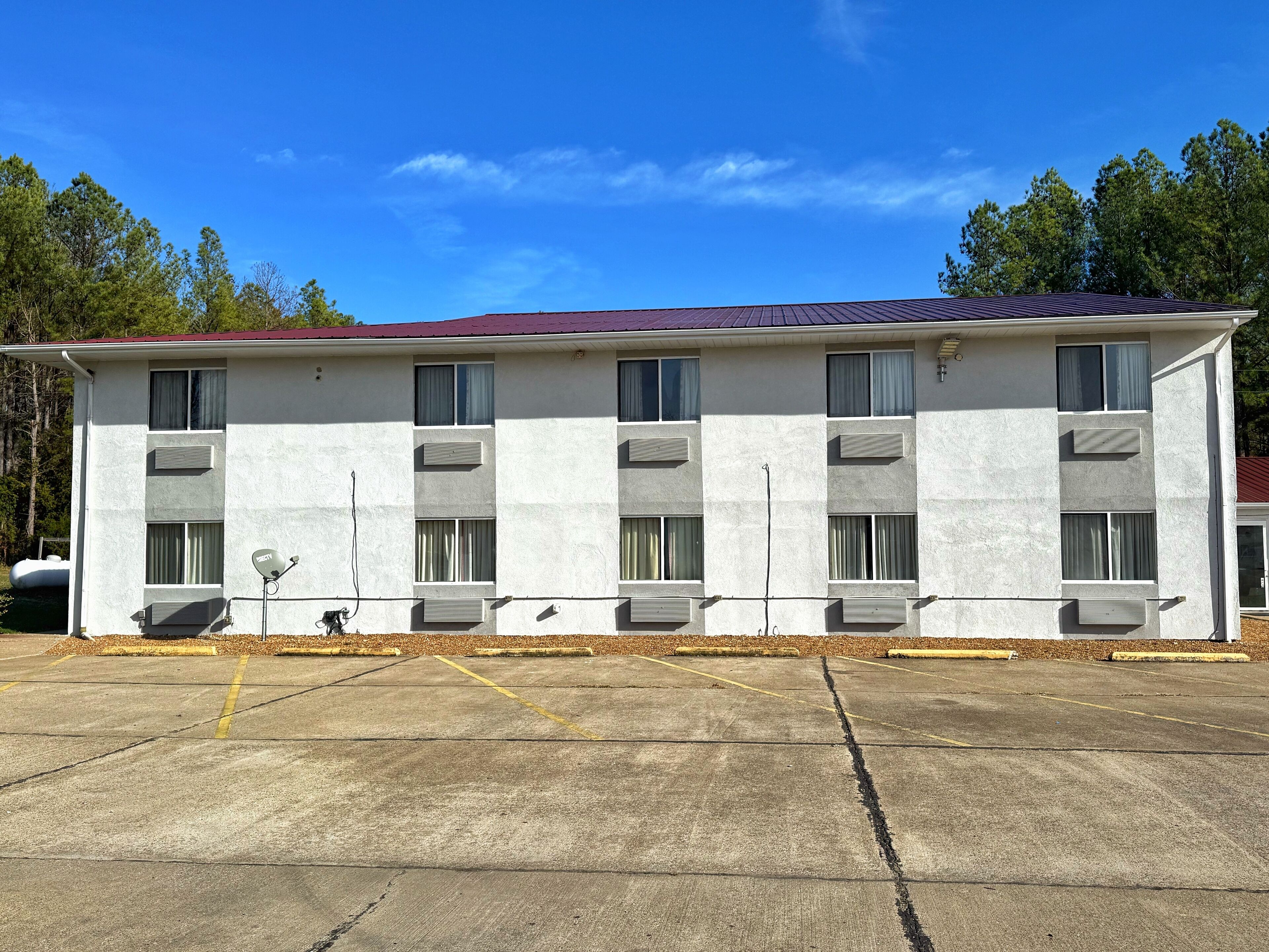 Un motel de varios pisos con techo rojo, unidades de aire acondicionado y un estacionamiento.