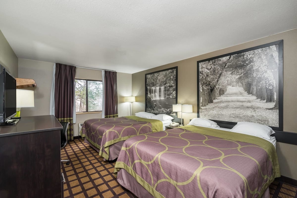 A hotel room with two beds, a desk, a TV, and large framed pictures on the walls.