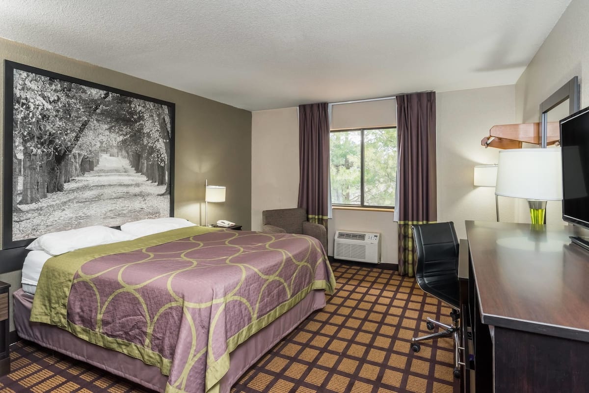 A hotel room with a large bed, a desk, a chair, a TV, and a window with curtains.