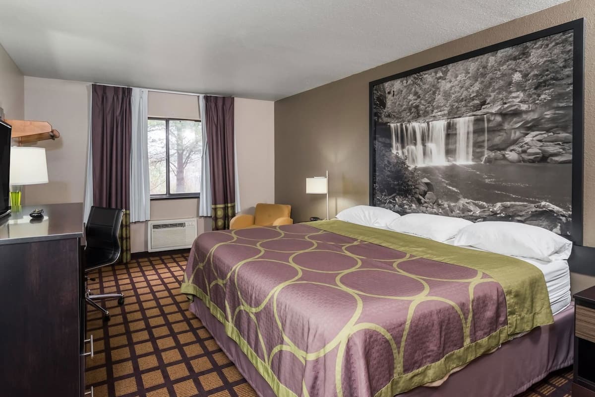 A hotel room with a bed, a desk, a chair, a window with curtains, and a large wall-mounted picture of a waterfall.