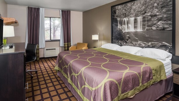 A hotel room with a bed, a desk, a chair, a window with curtains, and a large wall-mounted picture of a waterfall. - Super 8 by Wyndham Munfordville KY (Munfordville)