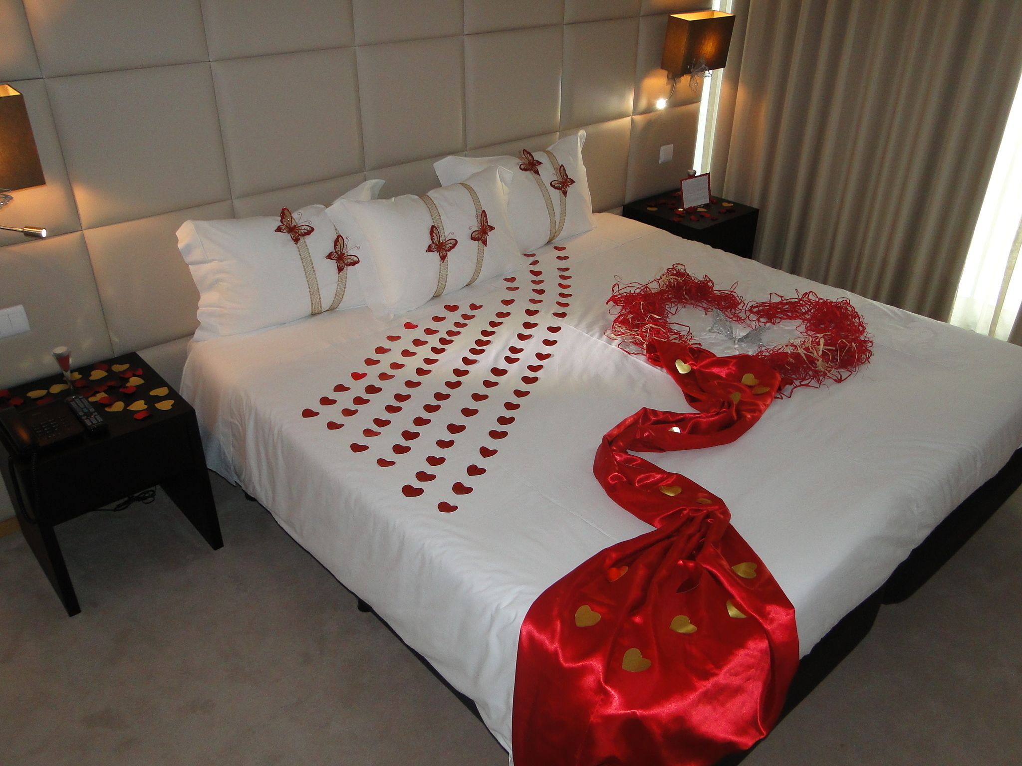 Una cama bien hecha con una decoración con forma de corazón y pétalos de rosa sobre el edredón.