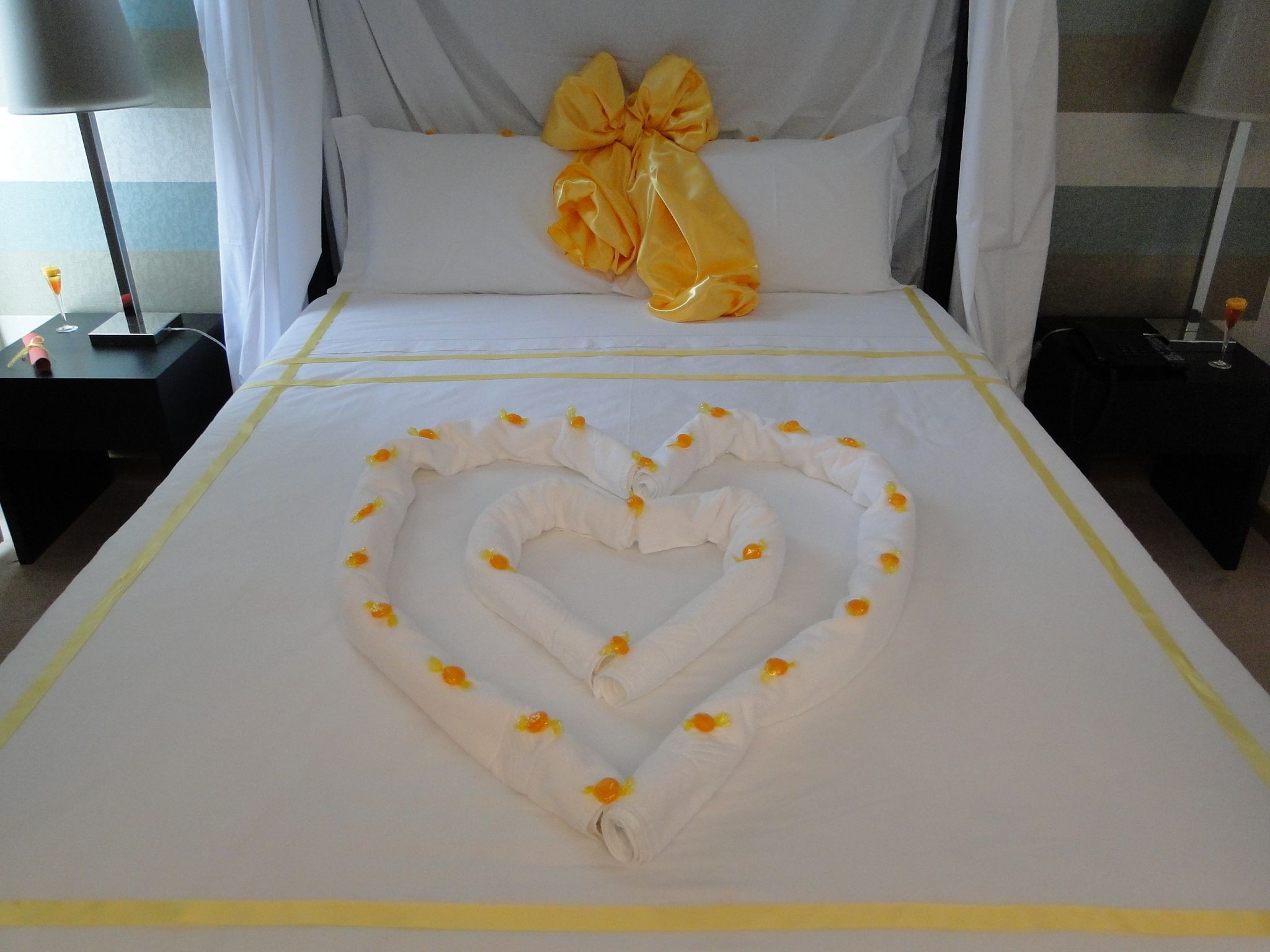 Un lit agrémenté d’une décoration en forme de cœur réalisée avec des serviettes et d’un grand oreiller en forme de nœud.
