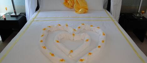 Una cama con una toalla dispuesta en forma de corazón y una almohada con un lazo grande.