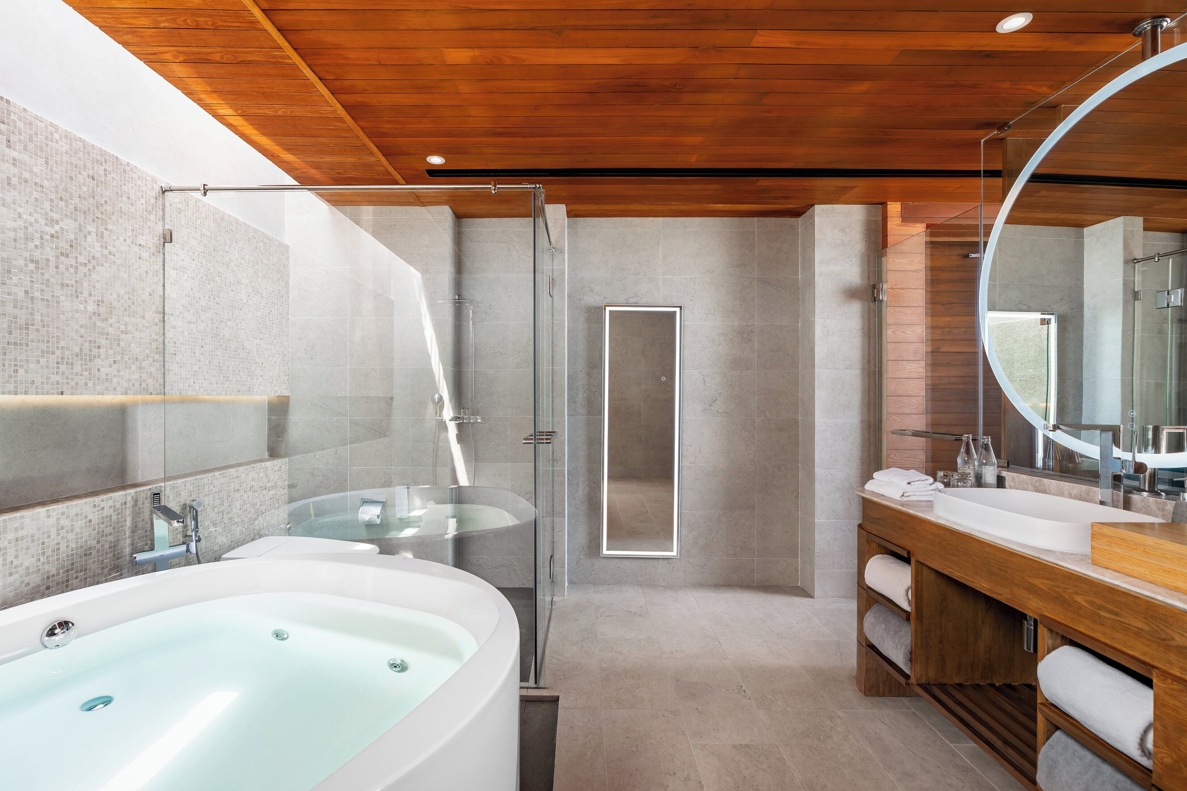 A modern bathroom with a large bathtub, a glass-enclosed shower, and a wooden vanity.