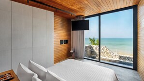 Un dormitorio moderno con una cama grande, un televisor en la pared y vista al mar a través de ventanales.