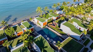 Un resort con varias villas, una piscina central y vista a la playa.