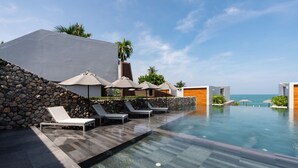 Un área de piscina moderna con sillones de descanso y sombrillas, un muro de piedra y vistas al océano.