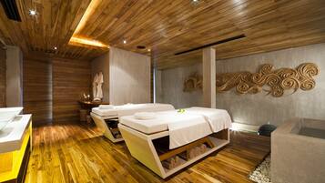 Un cuarto de spa con piso de madera, dos camillas de masaje, un lavamanos pequeño y un adorno en la pared.