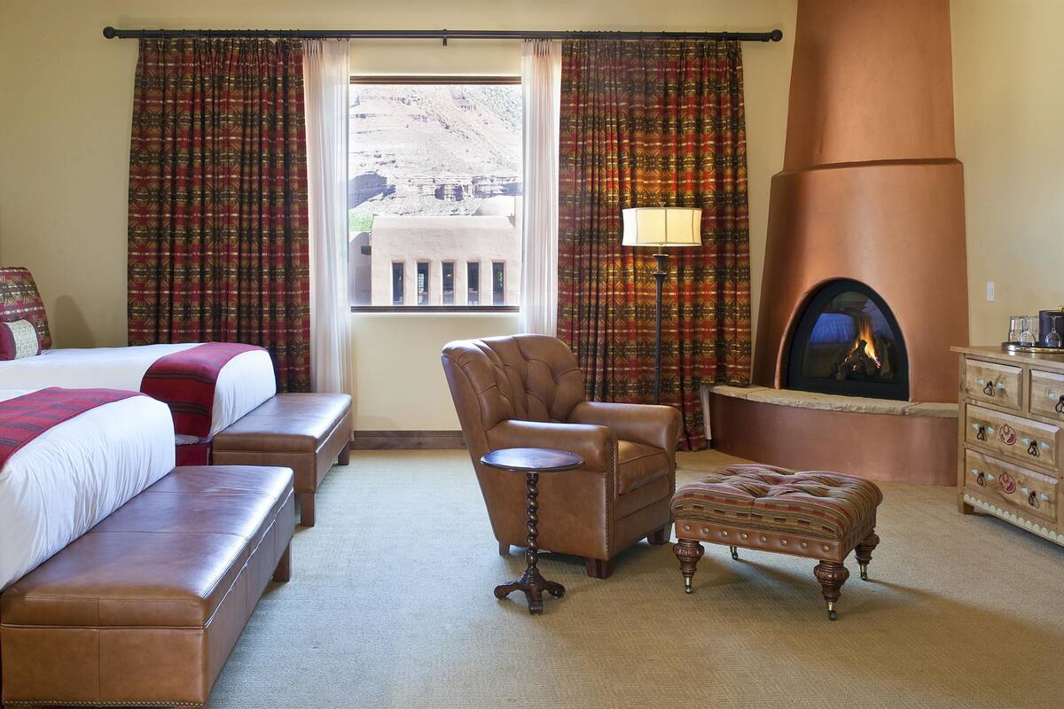 Une chambre d’hôtel avec deux lits, un canapé, un fauteuil, une cheminée et une commode.