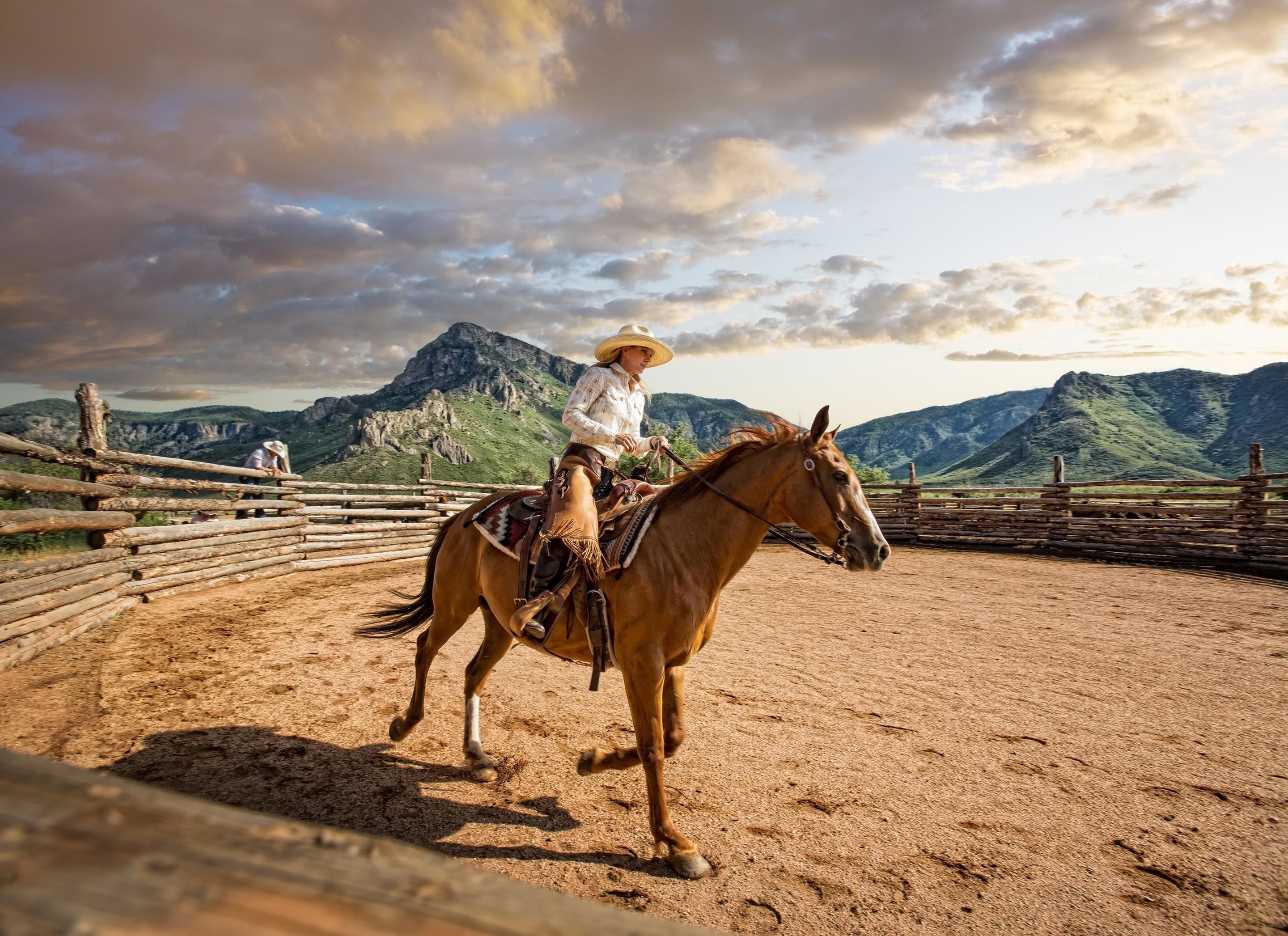 A person riding a horse in an outdoor arena with a mountainous backdrop.