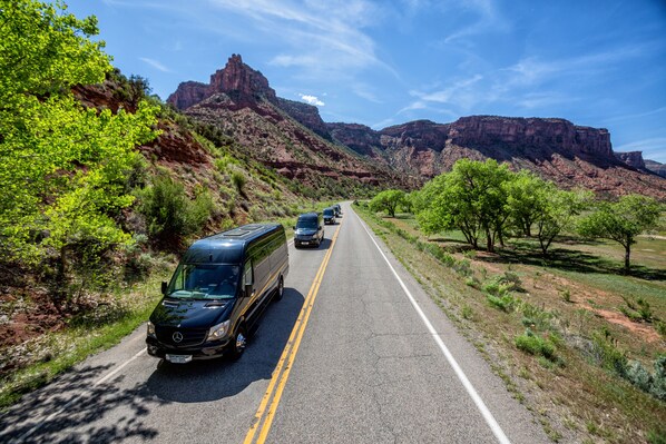 A highway with a van and cars, surrounded by green vegetation and red rock formations.