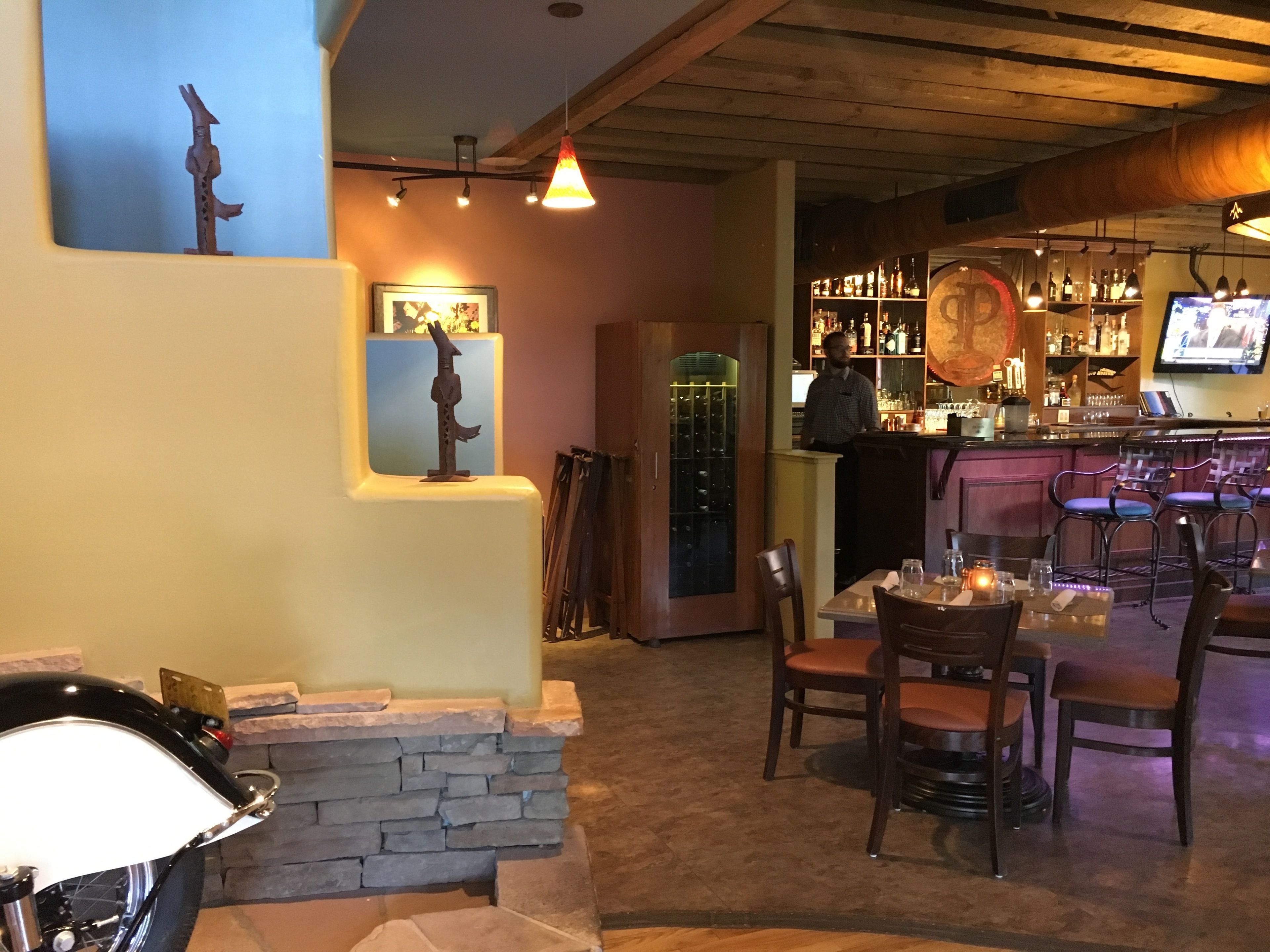Zona de bar con mostrador, taburetes y una pantalla de televisión. Hay una chimenea con revestimiento de piedra y una motocicleta estacionada afuera.