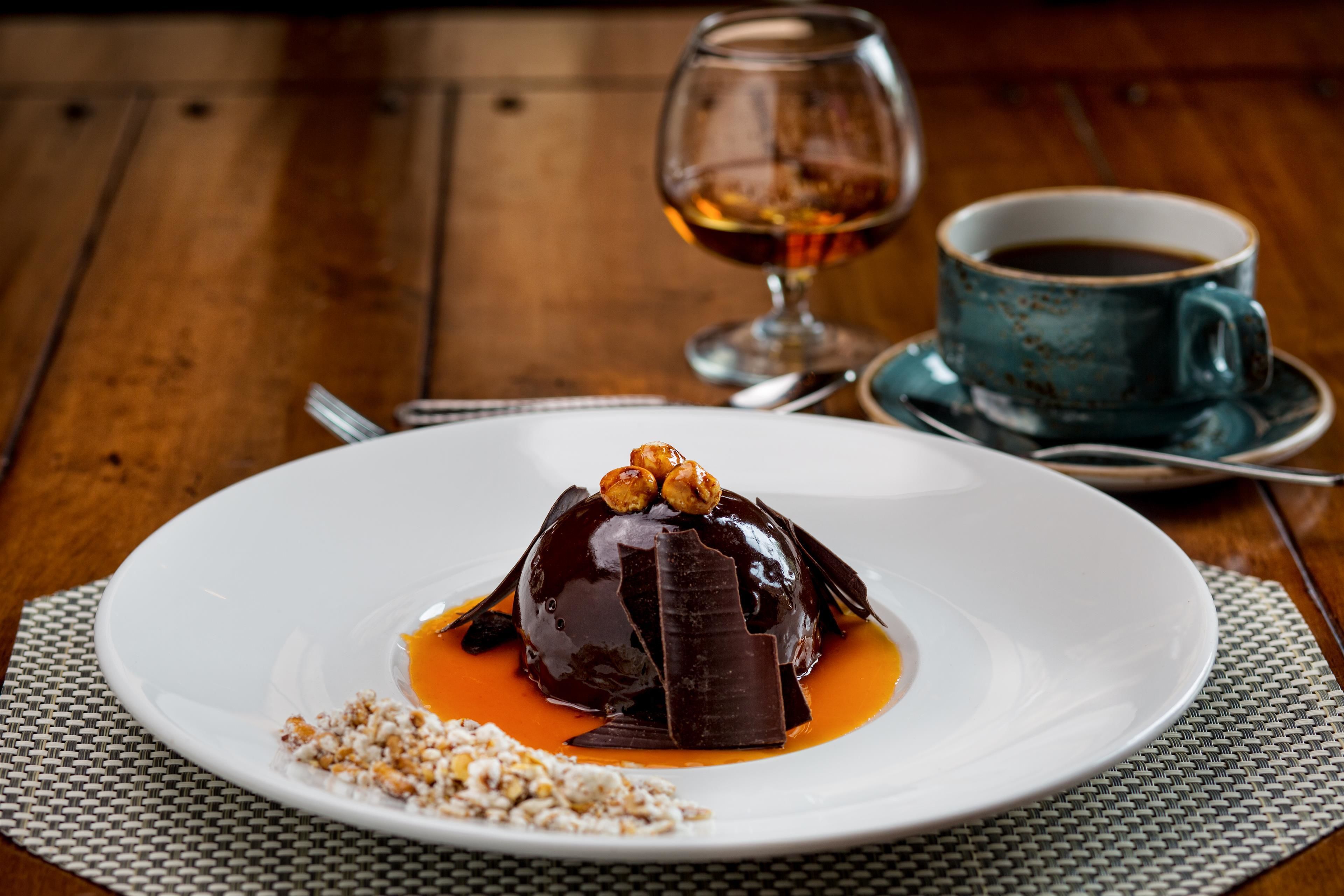 A dessert on a white plate with a glass of amber liquid and a cup of black liquid in the background.