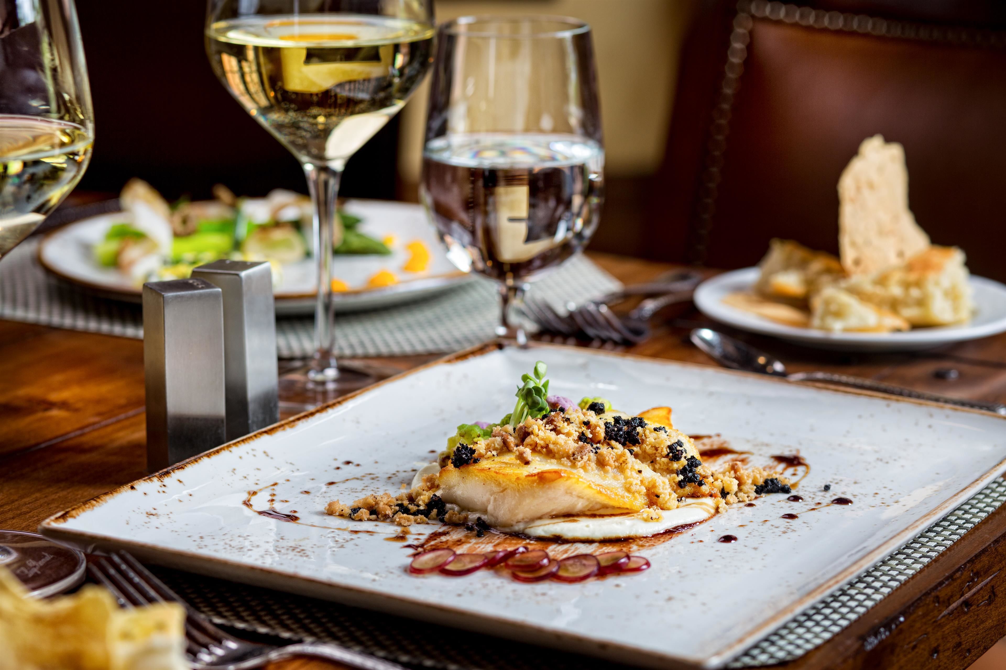 A dining table with a plate of food, a glass of white wine, and a glass of water.